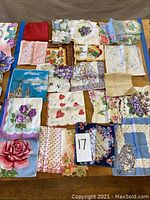 Overview of all 19 vintage women's linen handkerchiefs laid out, showing various floral, heart, cherub, animal, and harbor designs with some embroidered and scalloped edges.