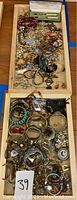 Overview photo of two trays with mixed costume jewelry pieces including watches, bracelets, pins, necklaces, earrings and pens.