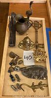 Wide view of lot showing brass pitcher with bird head handle, large ornate key, pig mold, bells, and various small figurines and objects.