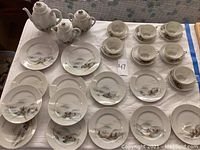 Full table layout showing all porcelain pieces including plates, cups, saucers, teapots and other serving pieces with scenic Japanese mountain landscape designs.
