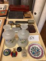 Overview photo showing large frosted Bristol glass vases with painted floral design, assorted small antique boxes and bottles, and sewing accessories on a wooden tray
