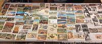 Wide assortment of postcards laid on a table showing various scenic, historical, and advertising images.