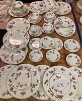 Full view of the assorted plates, bowls, cups, and saucers laid out on a wooden table showing the floral motifs and quantity.