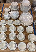 Arrangement of cups, saucers, plates, platters on wooden table showcasing the full set and pattern.