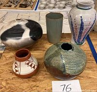 Five assorted studio pottery vases arranged on wood surface showing overall items in lot