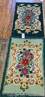 Pair of vintage hand-hooked rugs placed on wooden floor showing floral central designs with decorative borders.