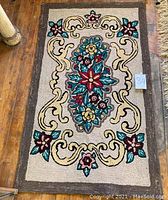 Full view of the vintage hand-hooked rug showing floral and scroll pattern with a dark border.