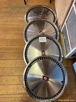 Four vintage Oldsmobile stainless steel hub caps stacked on wood floor, showing front surfaces and overall condition.