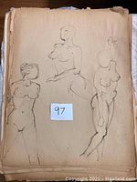 Photo of several nude female figure sketches on aged paper showing pencil and charcoal work.