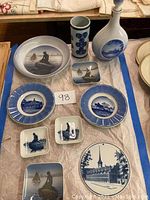 Overview of entire collection arranged on a cloth, showing plates, dishes, vase, and decanter with Danish blue and white motifs including the Little Mermaid and architecture.