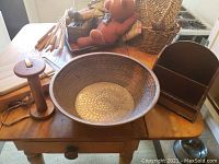 Photo showing large hammered copper bowl on a wooden table alongside other items including a wooden house organizer and tall wooden spool towel holder.