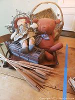 Photo showing Raggedy Ann doll, stuffed bear, and two woven baskets on a wooden table.