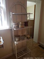 Full view of the four-level white metal bakers rack with various ceramic containers on shelves, showing overall structure and condition.