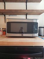 Front view of GE microwave oven showing stainless steel body and black windowed door on a wooden countertop.