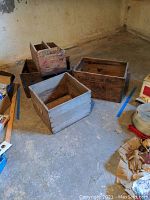 Photo showing all four vintage wooden crates grouped on a concrete floor in a basement, displaying varying sizes and weathered wood surfaces.