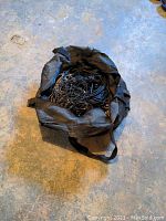 Black travel bag filled with numerous cords and cables lying on a concrete floor.