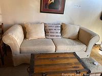 Front view of beige fabric sofa with three cushions and decorative pillow with text, in living room setting.