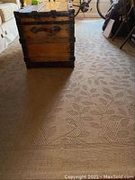 Long shot showing the sisal rug with a floral pattern under a wooden chest and part of a bicycle in a room, beige color, textured surface