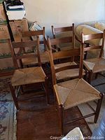 Set of six ladder back wooden dining chairs with woven natural fiber seats, two have arms (captains chairs).