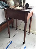 Full view of antique wooden nightstand table showing rectangular top and turned legs with scratches on finish.