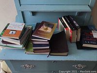 Image showing multiple books stacked and spread on a blue wooden surface including bibles, devotional titles, and other assorted books.