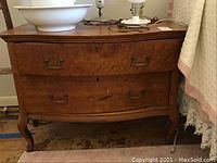 Front view of antique two drawer dresser showing wood grain, curved legs, and metal handles on drawers, with visible scratches and chips.