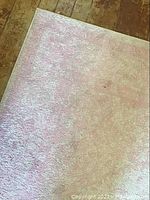 Photo showing corner of the lilac colored area rug with subtle border and texture.