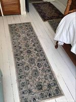 Long narrow runner with floral medallion patterns in gray tones laid on white wooden floor near bed and door