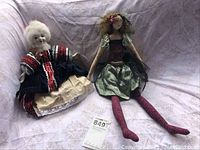 Both dolls sitting side by side on fabric backdrop showing size and outfit styles
