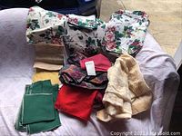 Lot showing two floral patterned table cloths with pink roses, green solid napkins, and various colored place mats and napkins arranged on a surface.