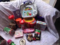 Full view of lot with various toys, bags, and collectible tins, boxes, and figurines grouped together on a white sofa.