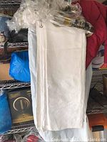 Two white tablecloths folded, stacked, and shown hanging, fabric visible with faint floral patterns.