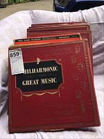 Photo of stack of red vinyl record albums titled Philharmonic Family Library of Great Music in varying volume numbers.