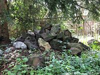 Pile of large landscaping rocks outdoors surrounded by plants, some dirt and moss visible on rocks.
