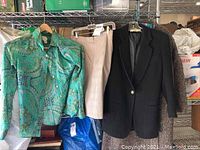 Front view of the three clothing items hanging on a rack: a green paisley silk shirt, a light pink skirt, and a black dress coat.