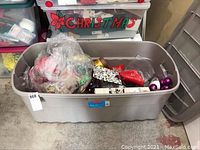 Large gray plastic bin filled with assorted Christmas decorations including ribbons, ornaments, and household items.