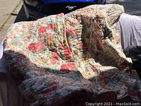 Quilted floral patchwork blanket with red and pink patterns draped outdoors in sunlight.