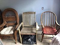 View of all three chairs together including wicker chair with white cushion, weathered teak chair, and antique wooden chair with red seat.