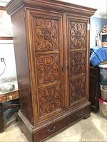 Front view showing two large carved panel doors, ornate wood details, and two bottom drawers with metal knobs.