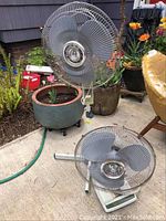 Two oscillating fans side by side, one standing and one laying down, with visible blade guards and chrome blade hubs.