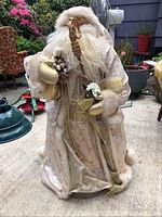 Full view of large Santa Claus figurine showing cream-colored robe, gold staff, sack with ornaments, and detailed beard and hair.