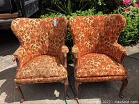 Front-facing image of two vintage wingback armchairs upholstered in orange-brown floral fabric showing wear and needing recovery.