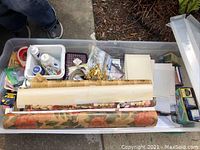 Overview photo showing multiple rolls of wrapping paper, white plastic bins with craft supplies, assorted papers, cards, and envelopes.