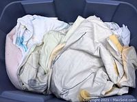 Loose assorted sheets in light colors including white, cream, and pastel shades, folded and wrinkled in a container.