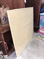 Full view of the blank 48x48 canvas leaning against furniture, showing overall size and condition.