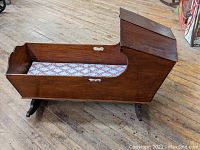 Side angle view of the walnut bonnet baby cradle showing the hooded top, rockers, and wooden construction.