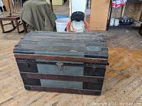 Front view of antique oak and tin trunk with lock and latch, showing wooden panels and metal reinforcements.