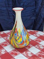 Front view of the vase showing multicolor swirl pattern and narrow neck with red rim on a checkered tablecloth.