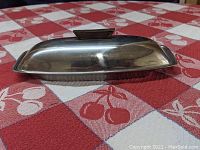 Side view of the mid-century modern stainless steel butter dish with walnut handle, showing sleek curved lid and base.