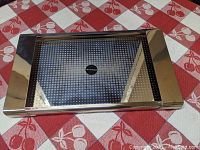 Top view of the polished stainless steel tray with perforated decorative center and Alessi logo plaque.